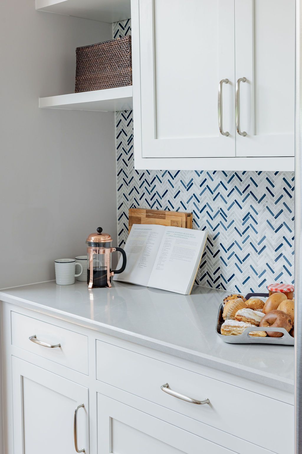 White kitchen cabinets with light countertops and a patterned backsplash; coffee and pastries displayed.