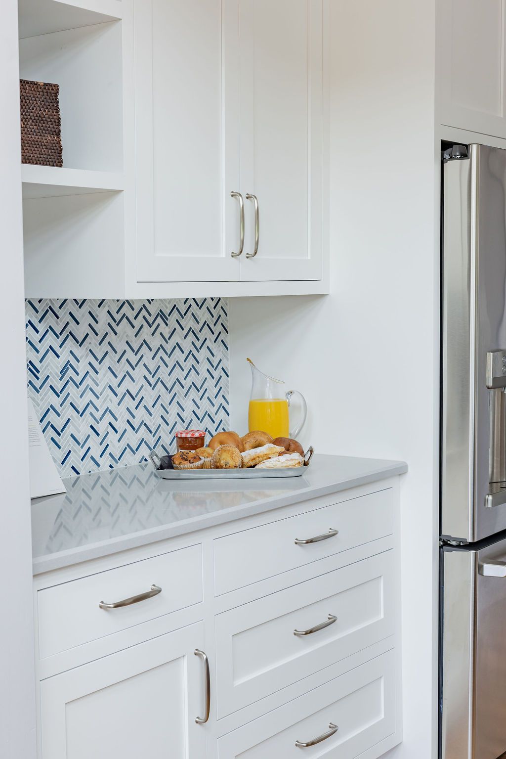 White kitchen corner with a mosaic backsplash, counter with food and drink, and cabinets.