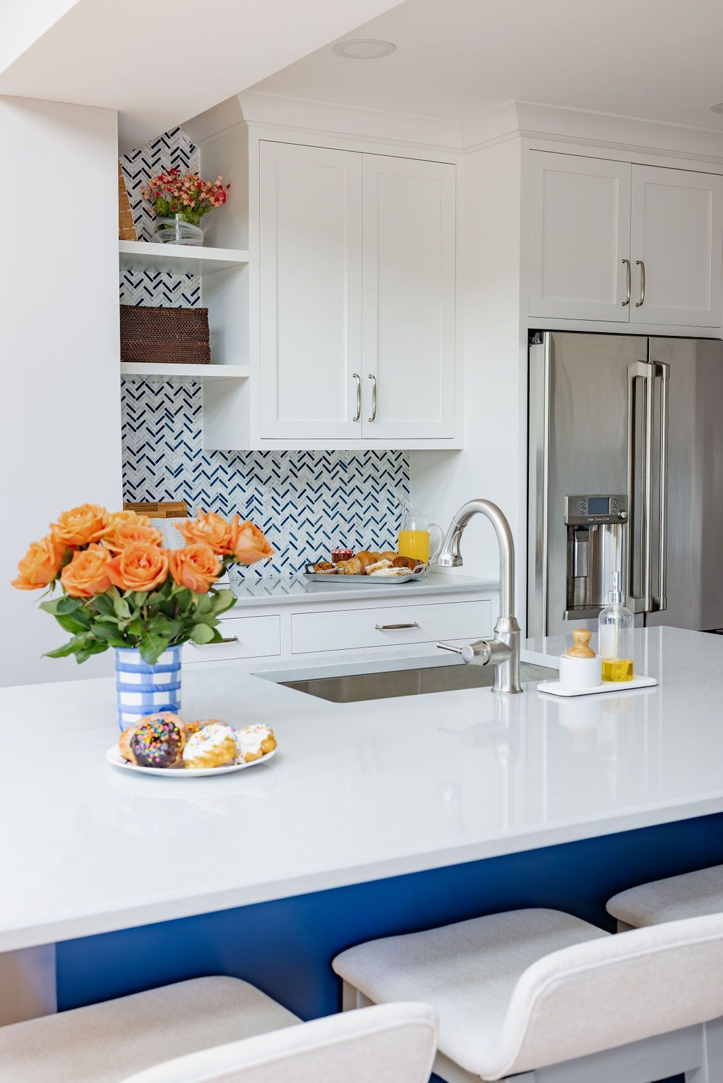 Kitchen with white cabinets, blue island, sink, and flowers. Donuts on a plate.