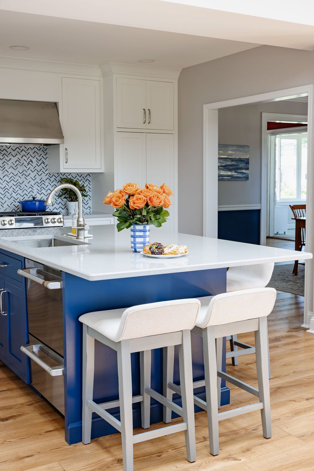 Kitchen island with blue cabinets, white countertop, and gray barstools. Orange flowers sit on the island.