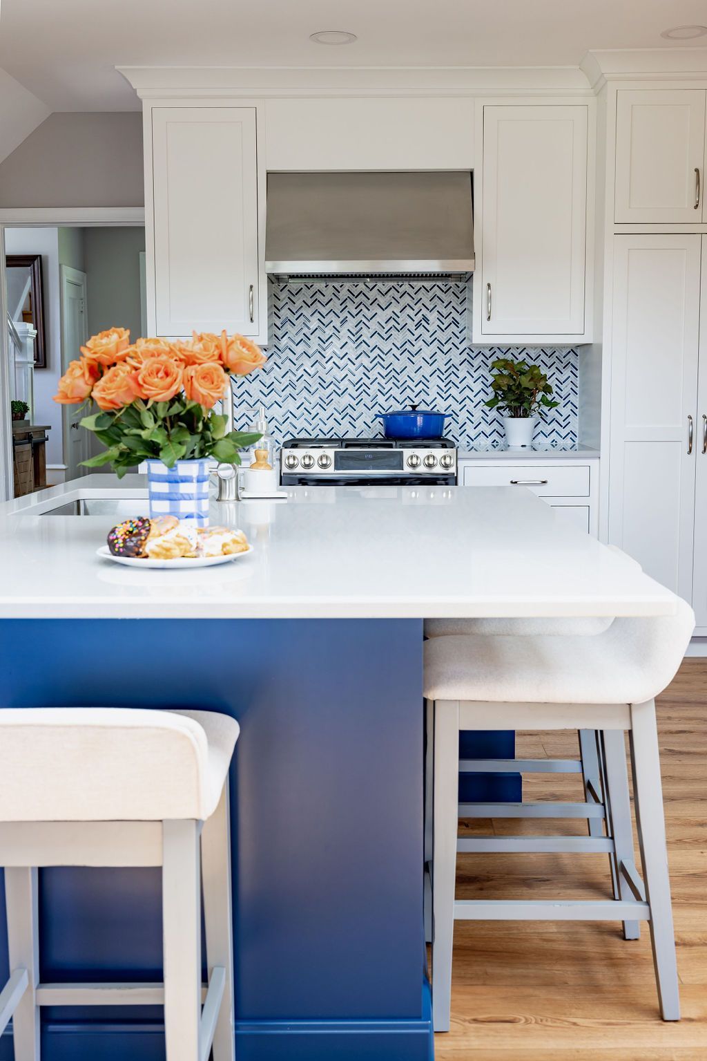 Kitchen island with blue base, white countertop, and white stools. Blue and white tiled backsplash.