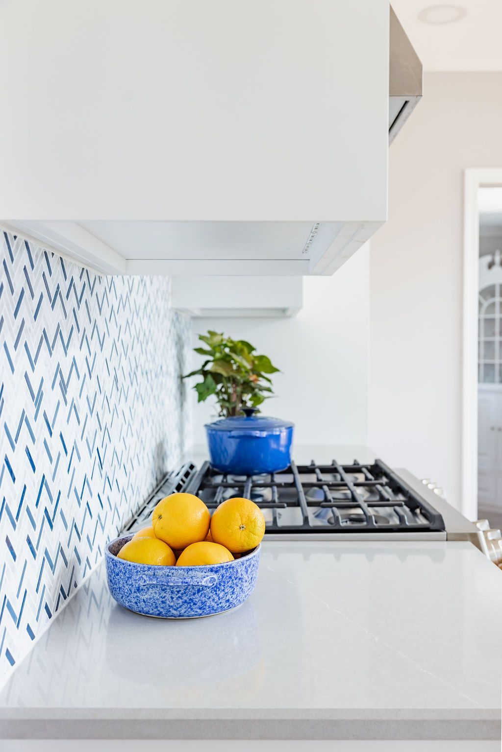 Kitchen countertop with blue mosaic backsplash, lemons in a blue bowl, and a gas cooktop.