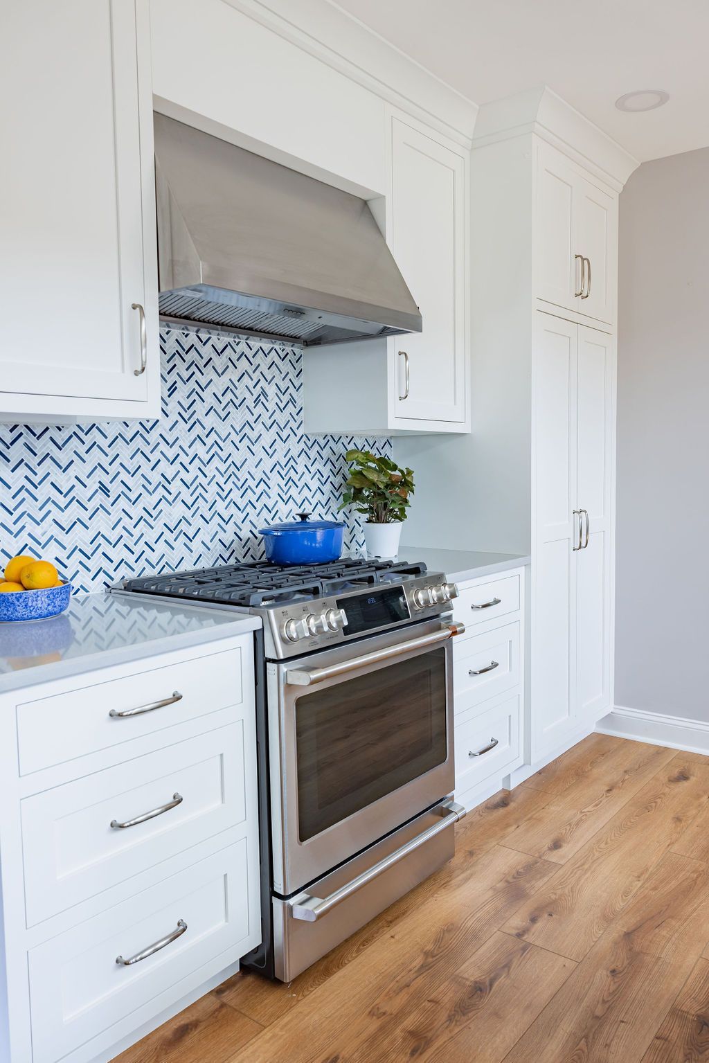 White kitchen with stainless steel oven, blue-tiled backsplash, and wood-look flooring.