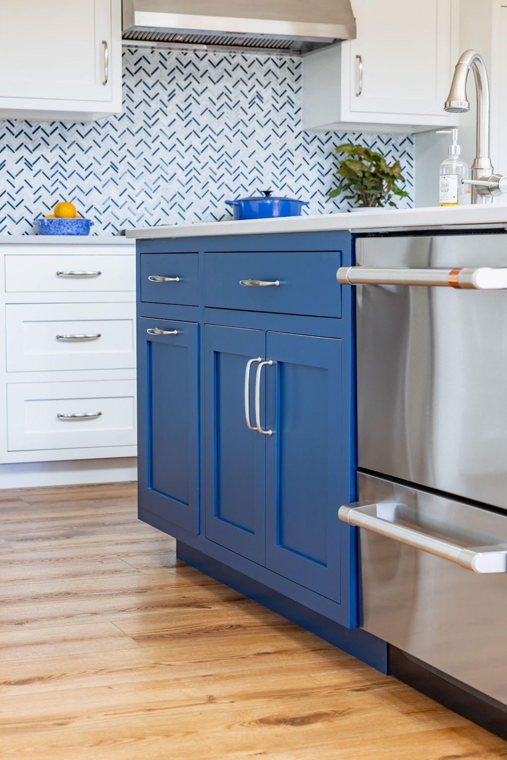 Blue kitchen island with stainless steel appliances and white cabinetry with a patterned backsplash.