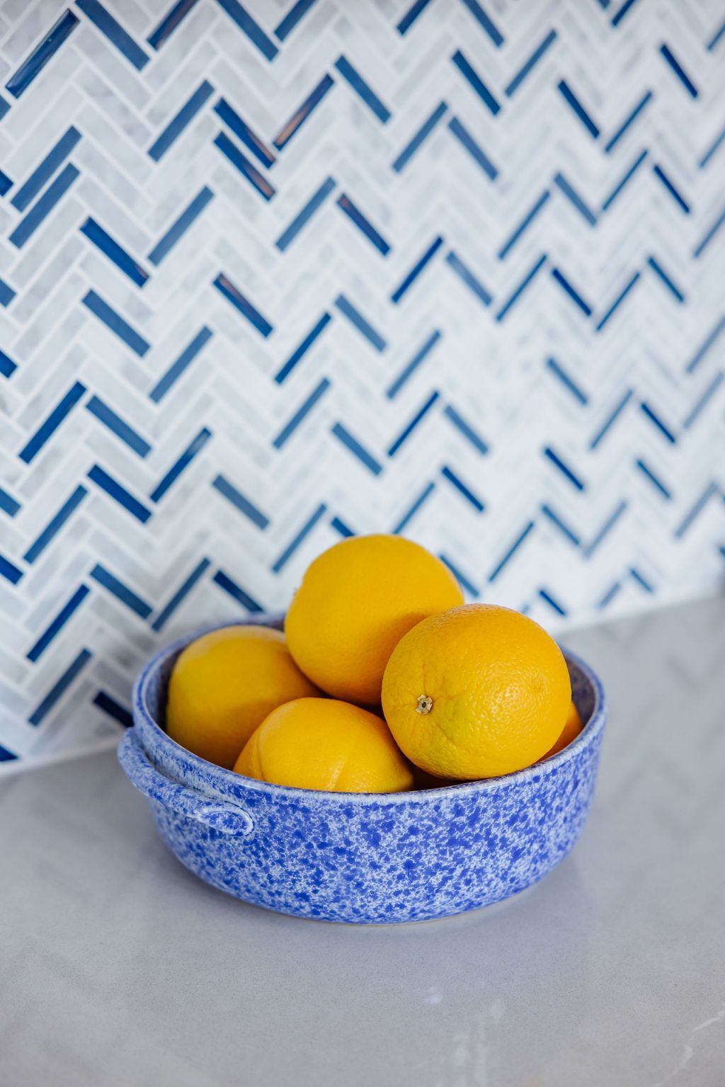 Bowl of lemons on a counter with blue and white herringbone tile backsplash.
