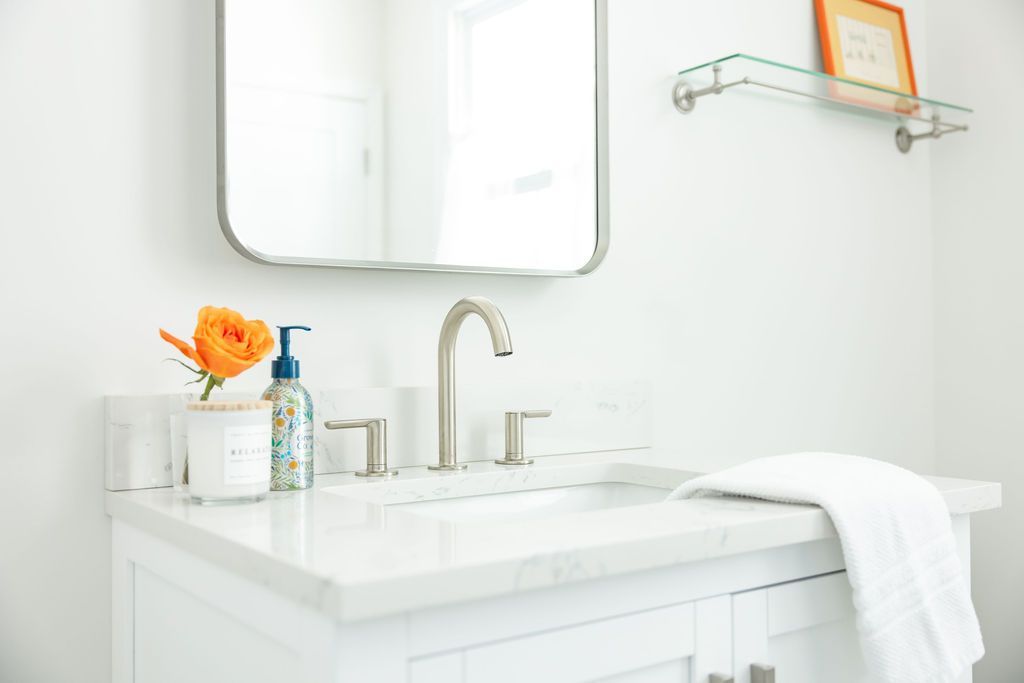 White bathroom sink with marble countertop, mirror, and decorative orange flower.