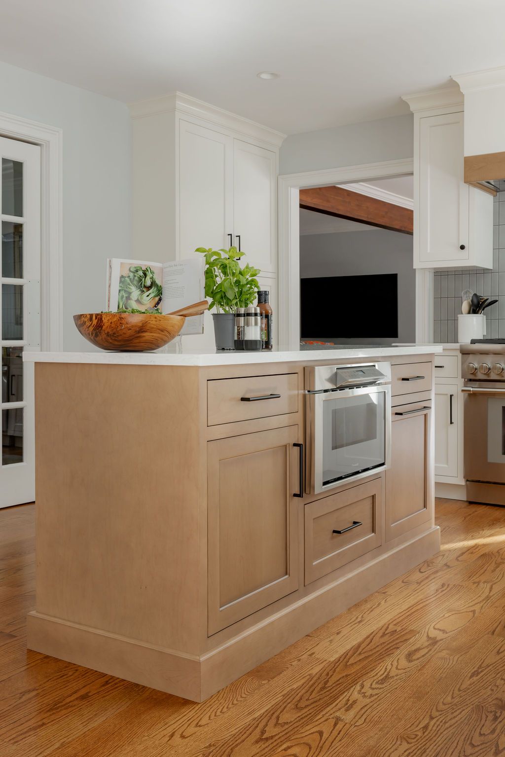 Kitchen island with built-in oven and drawers. Wooden cabinets, white countertop, hardwood floor, and white walls.