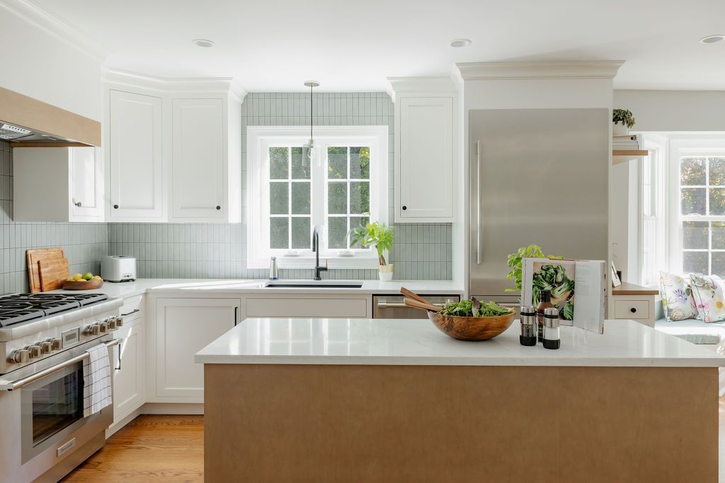 White kitchen with island, stainless steel appliances, and wood flooring.