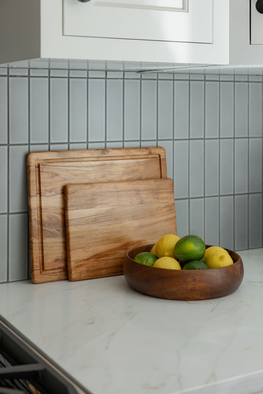 Two wooden cutting boards and a bowl of lemons and limes on a countertop, against a tiled backsplash.