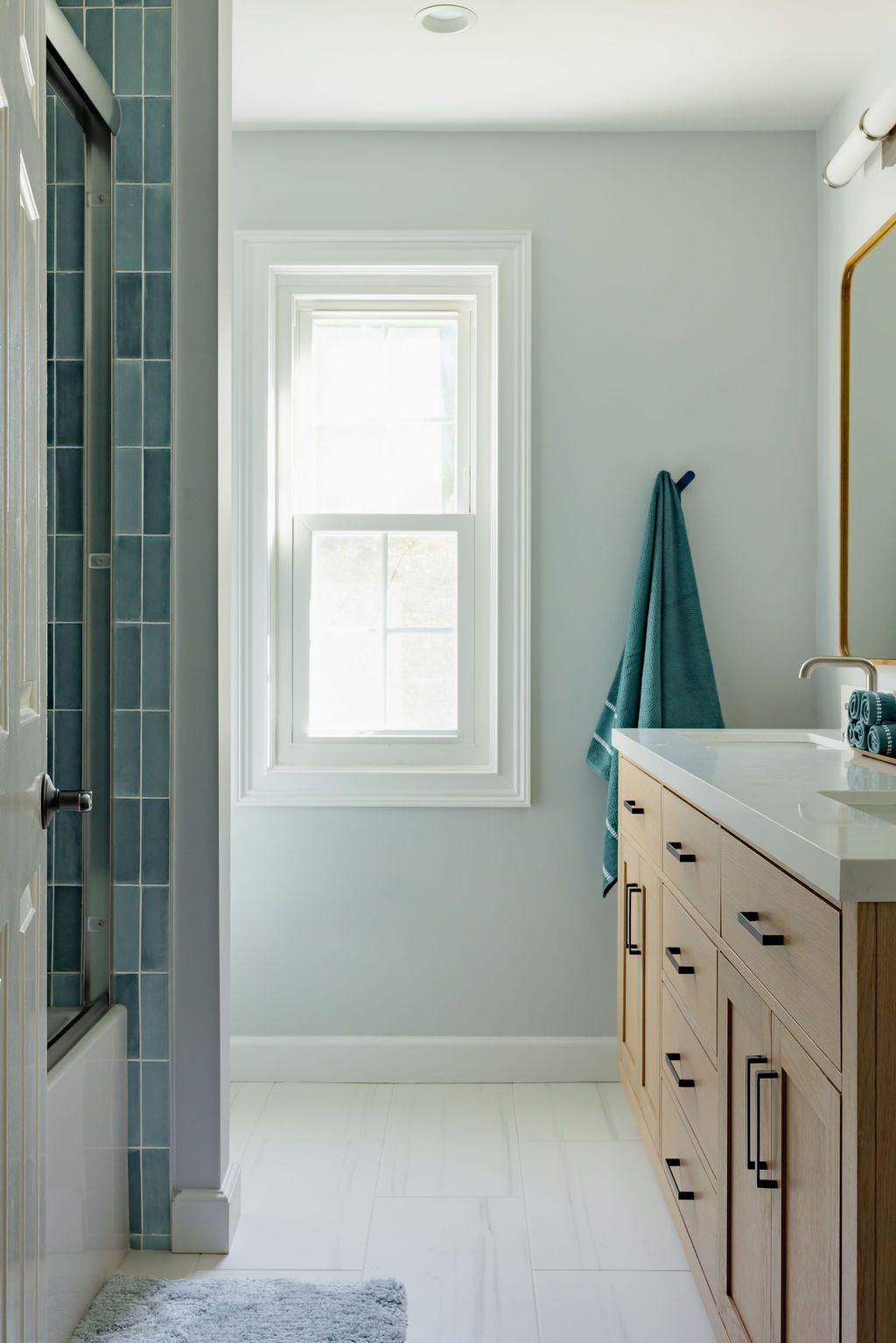 A light blue bathroom with a window, vanity, shower, and a towel.