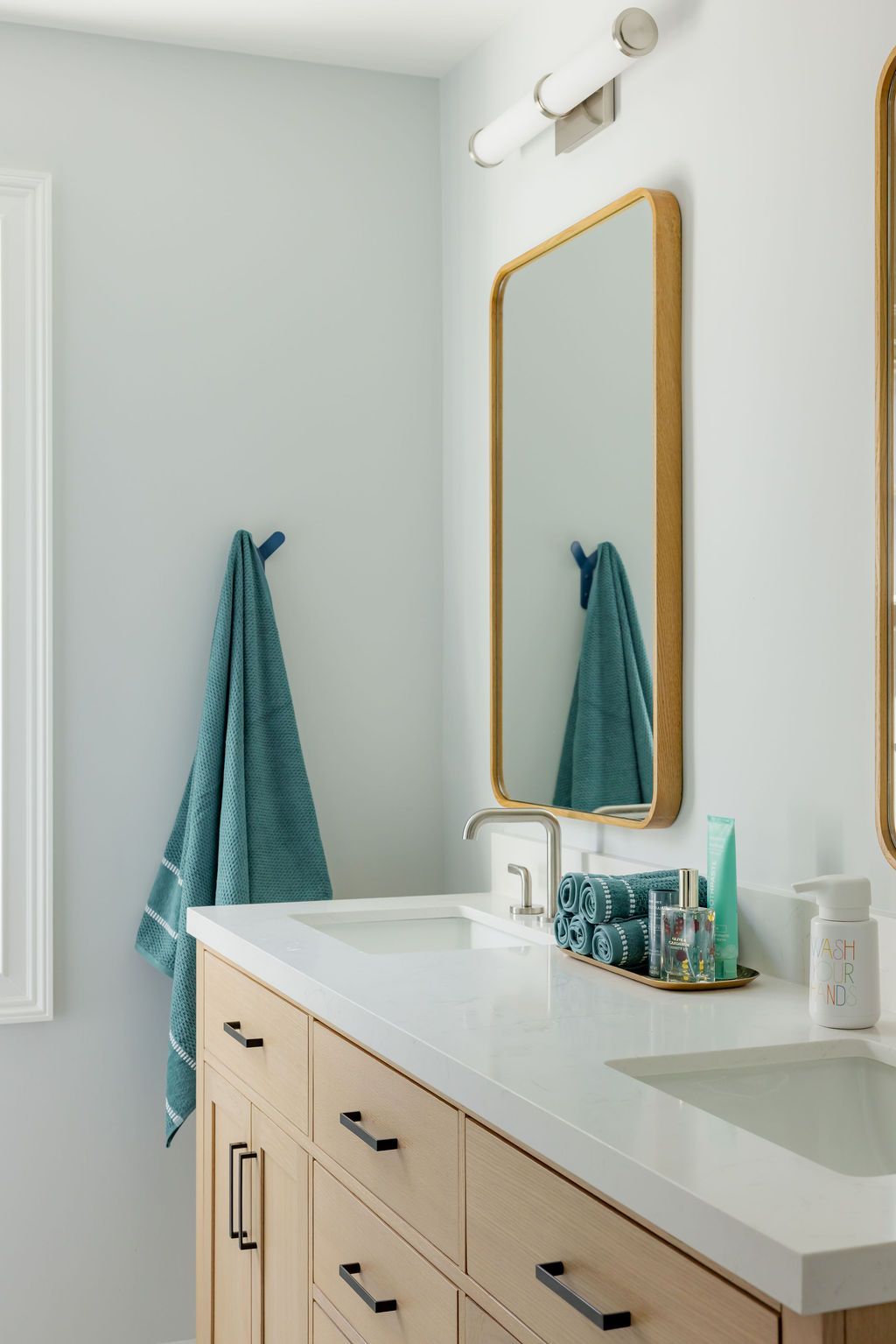 Bathroom with double sinks, gold mirror, turquoise towels, and light wood cabinetry.