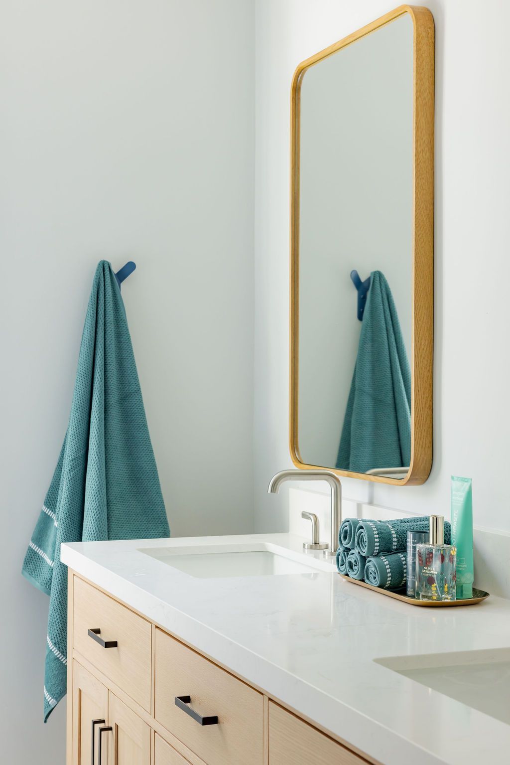 Bathroom with a light wood vanity, white countertop, and gold-framed mirror. A teal towel hangs from a hook.