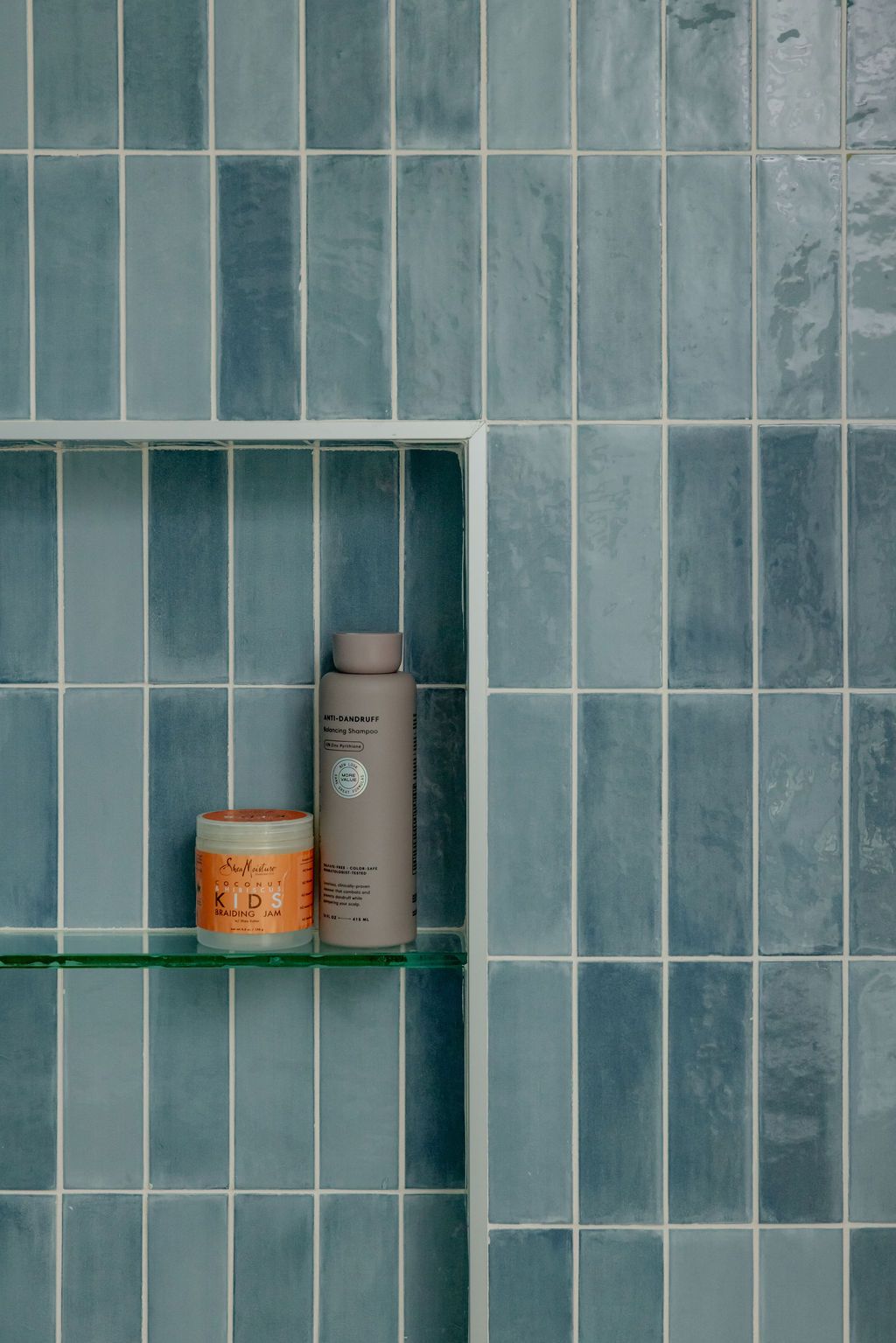 Blue tiled shower with a built-in shelf holding two cosmetic product containers.