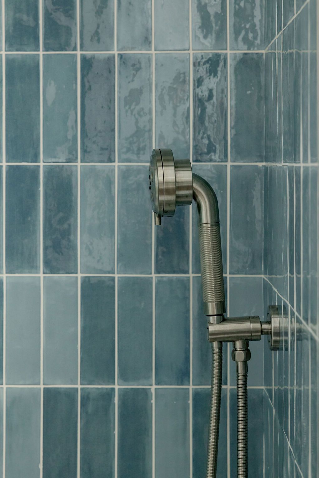Silver shower head on blue rectangular tiled wall.