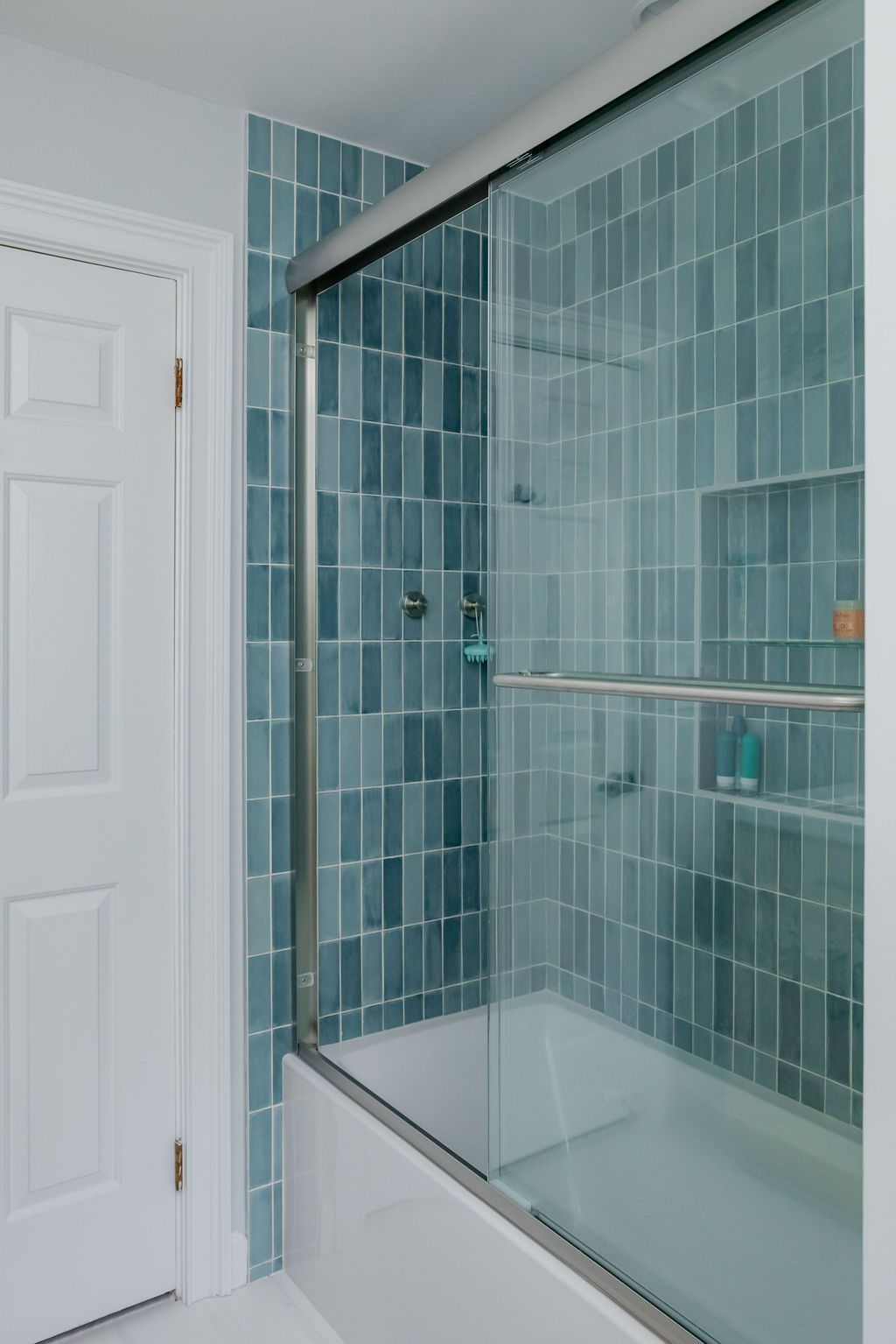 Blue tiled shower with sliding glass door in a white bathroom.