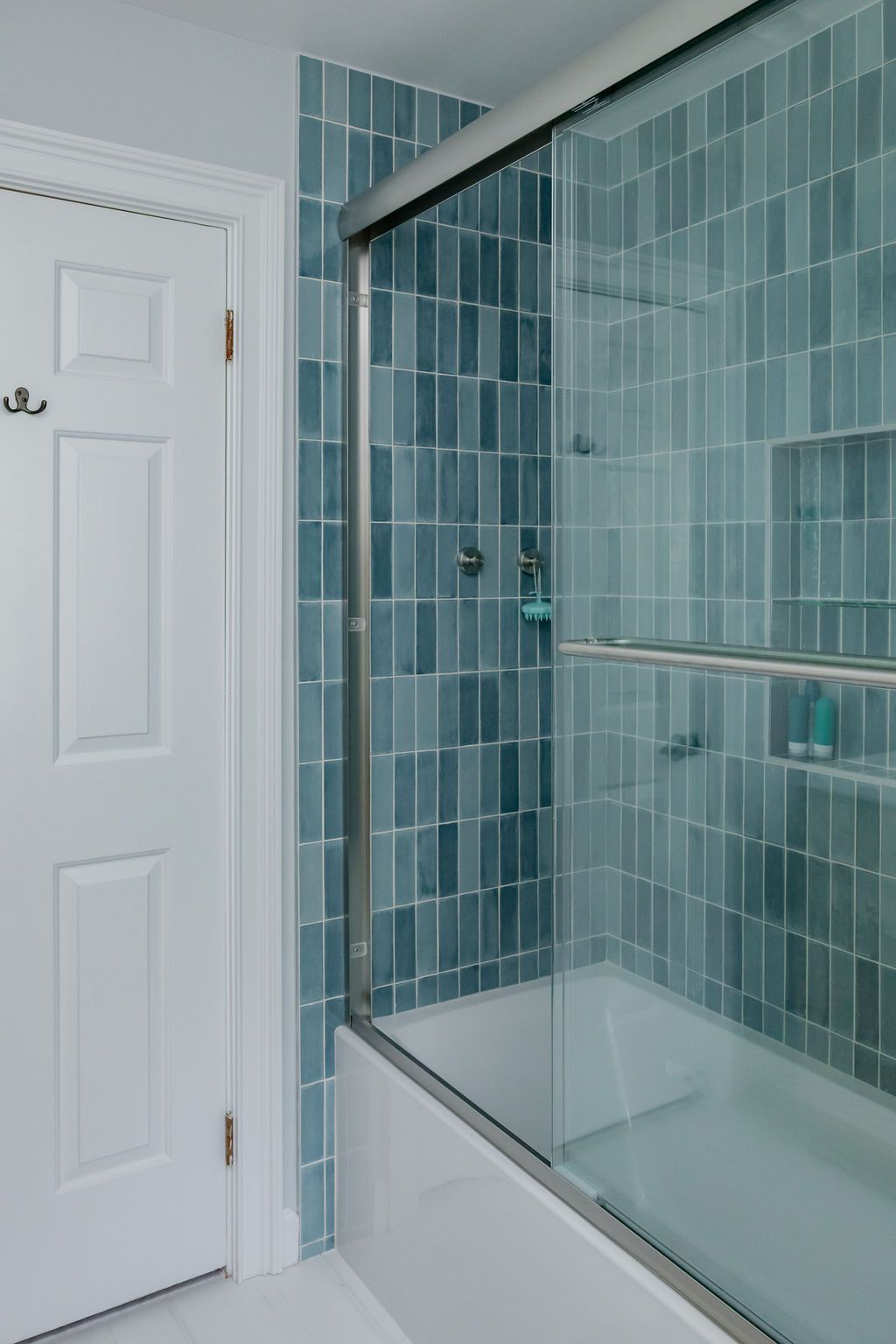 Bathroom with blue tiled shower, glass door, white tub and door.
