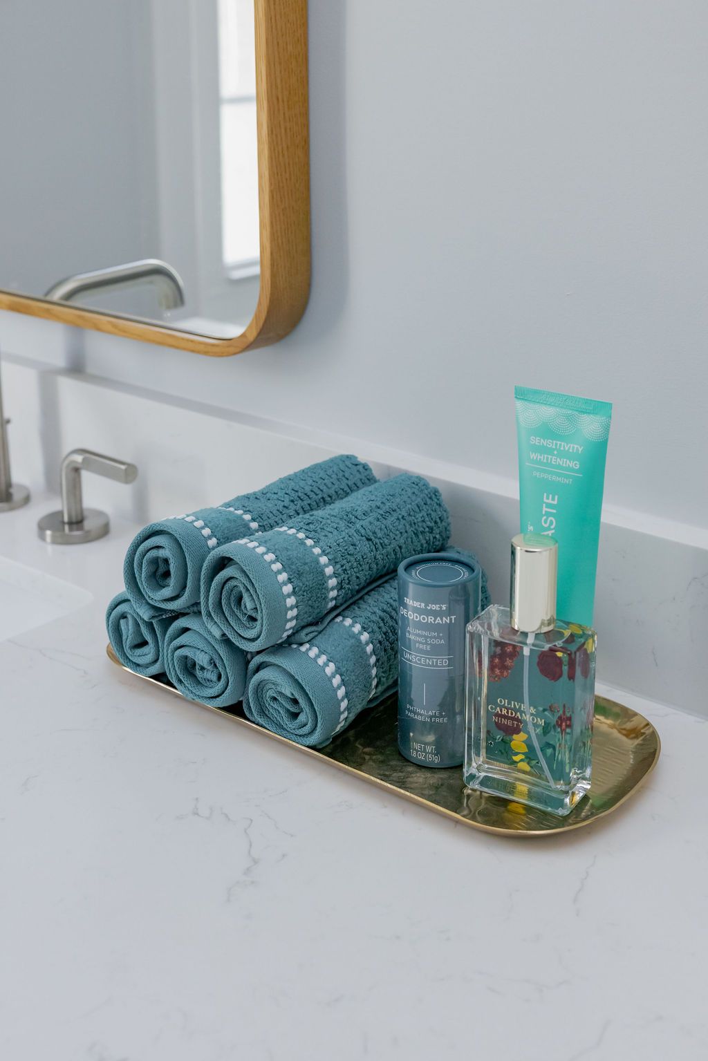 Blue towels, toiletries on a gold tray beside a sink. Mirror above.