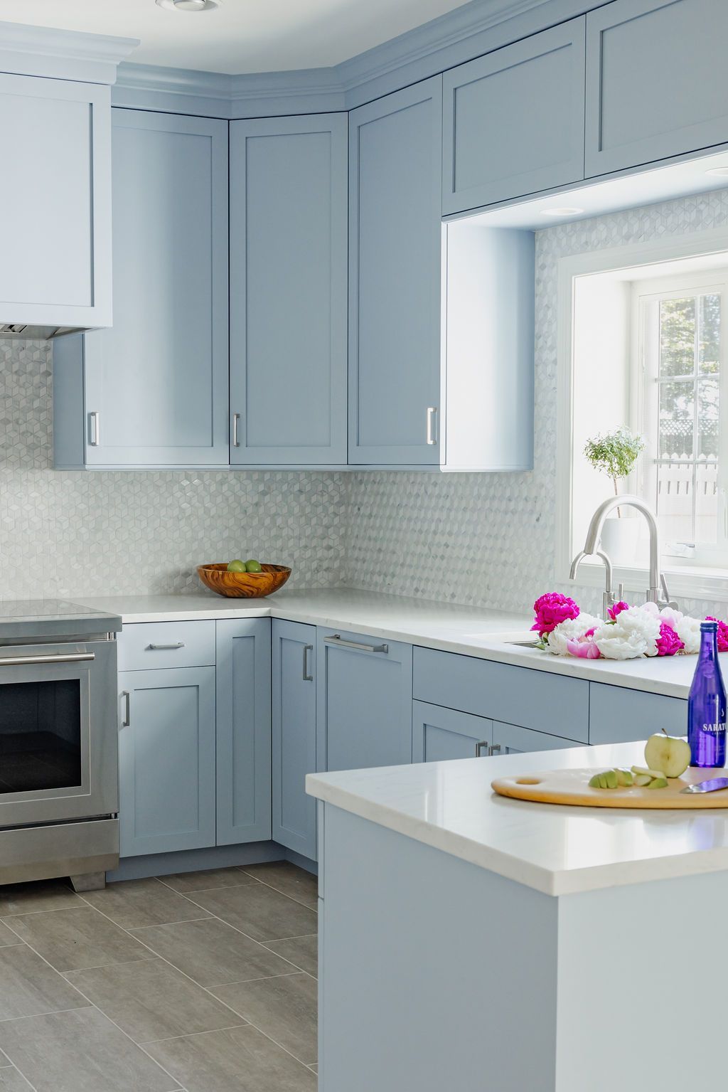 Blue kitchen with white countertops, backsplash, and island. Stainless steel oven. Flowers on the counter.