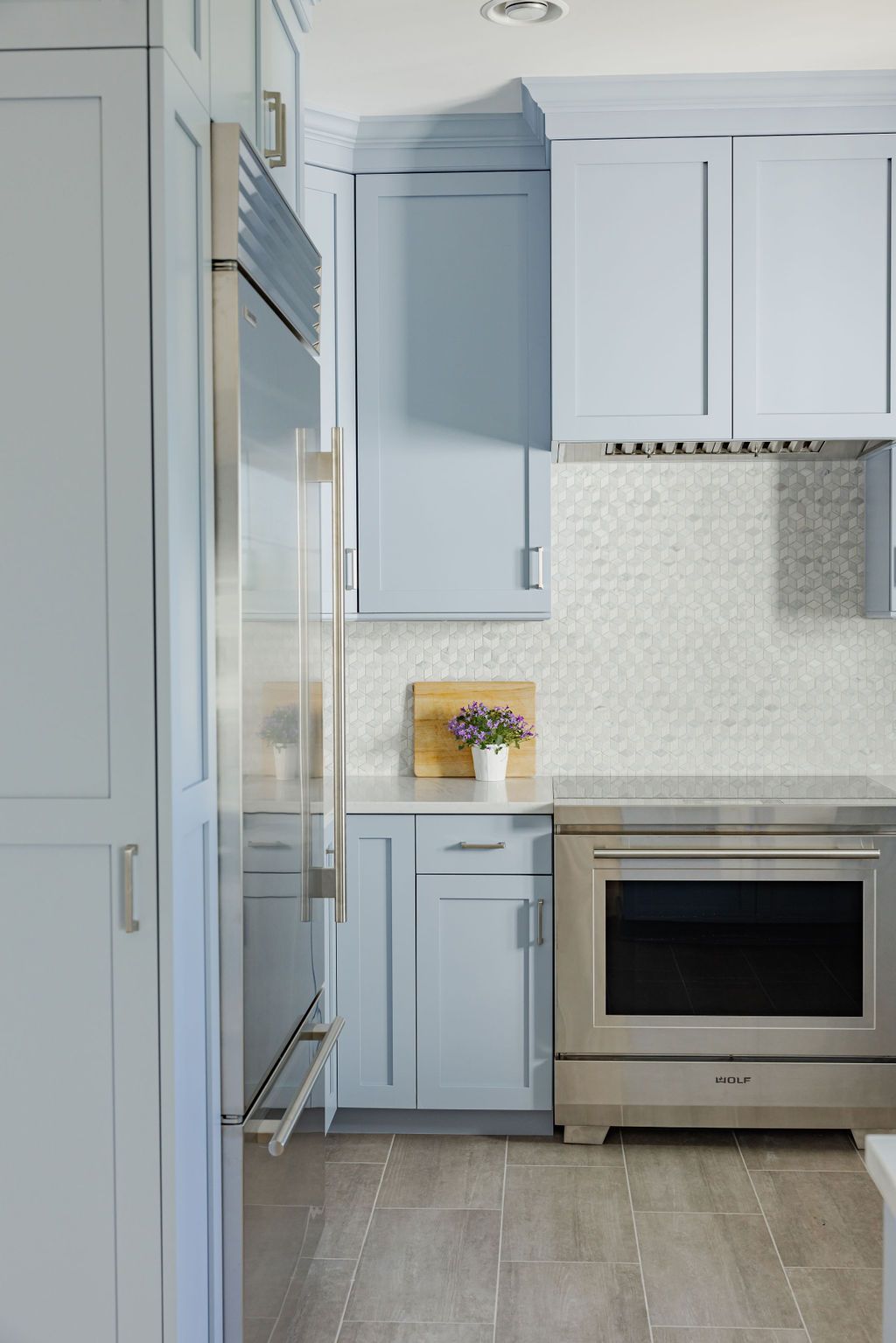Light blue kitchen with stainless steel appliances, mosaic tile backsplash, and light wood flooring.