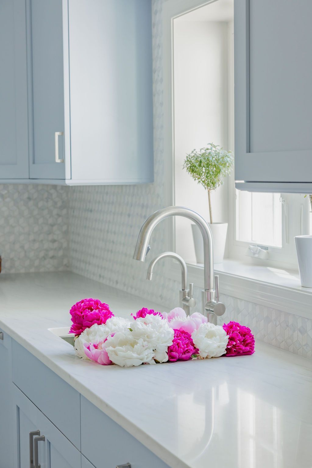 Kitchen with white countertop, blue cabinets, and pink and white peonies.