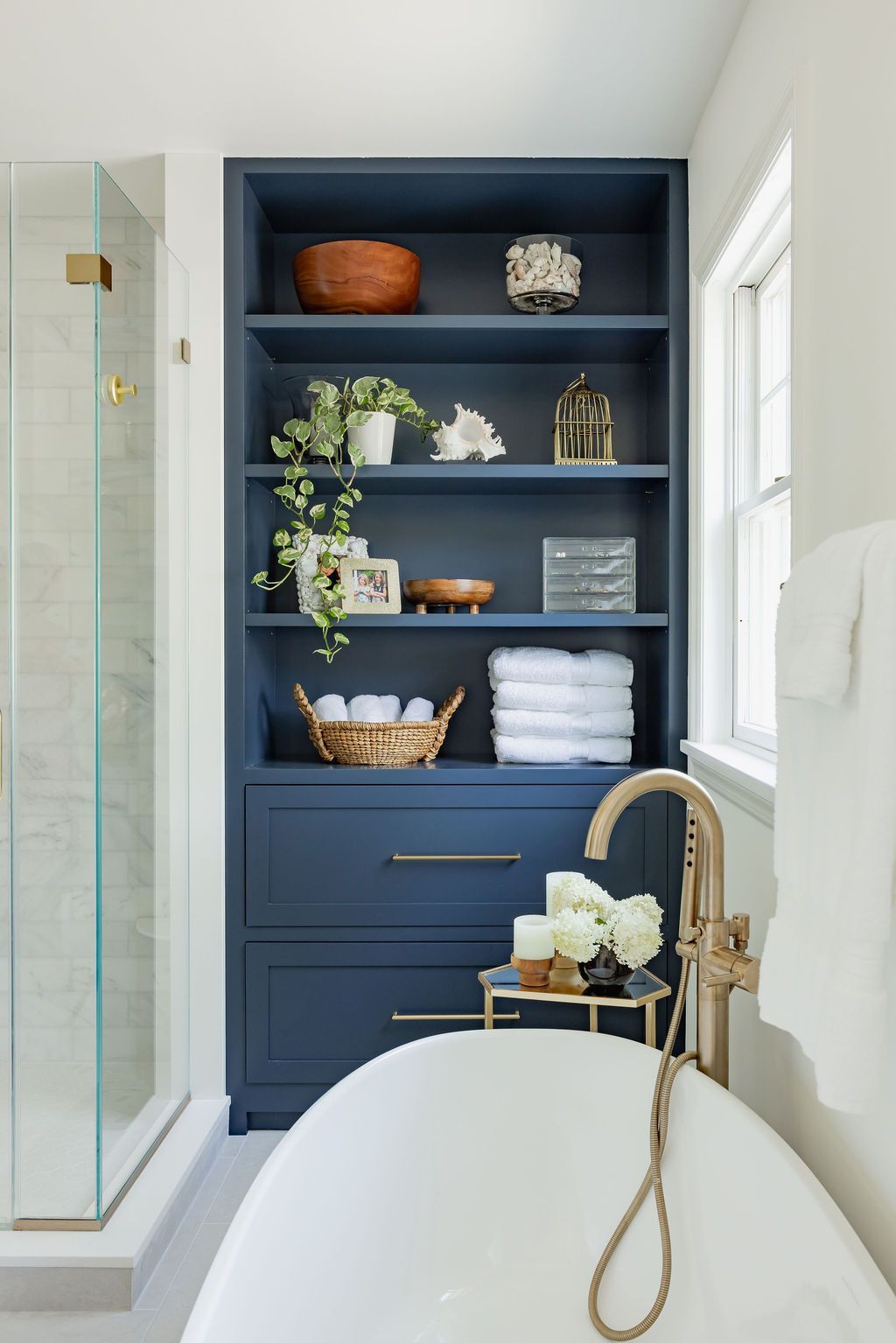 Bathroom with blue built-in shelving, a tub, gold fixtures, and white towels.