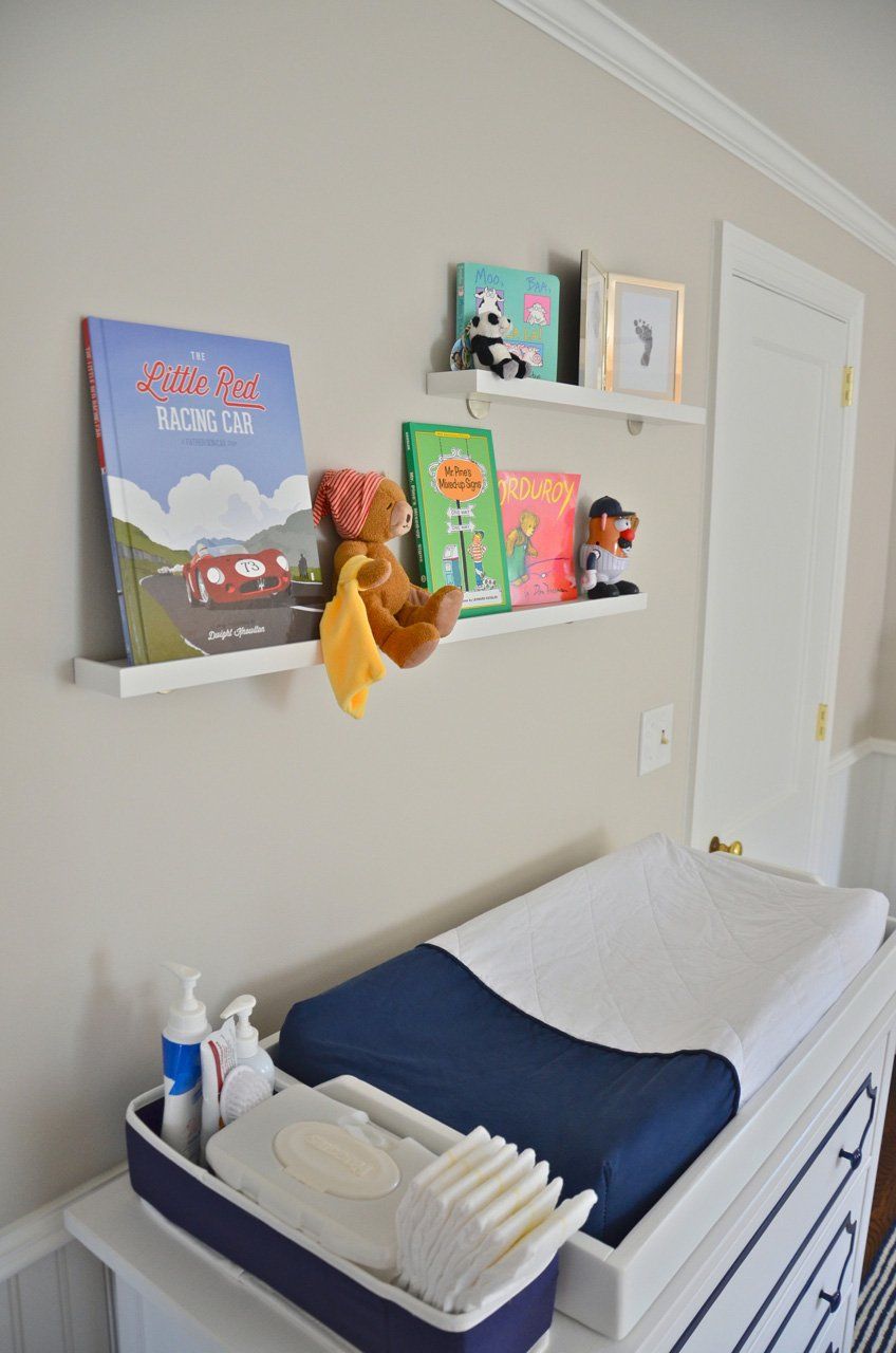 Nursery with white shelves holding books and toys above a changing table with supplies.