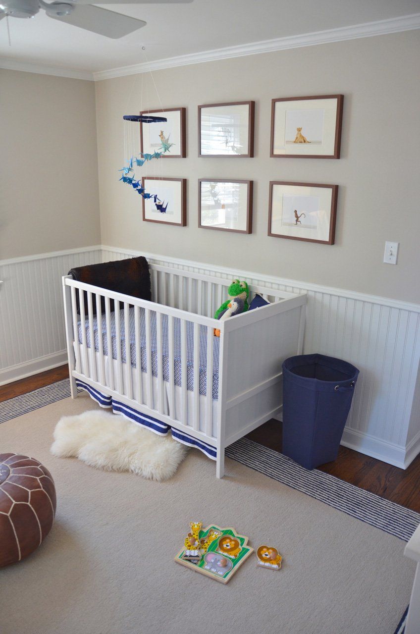 A white crib in a nursery with framed art, a blue trash can, and a sheepskin rug.
