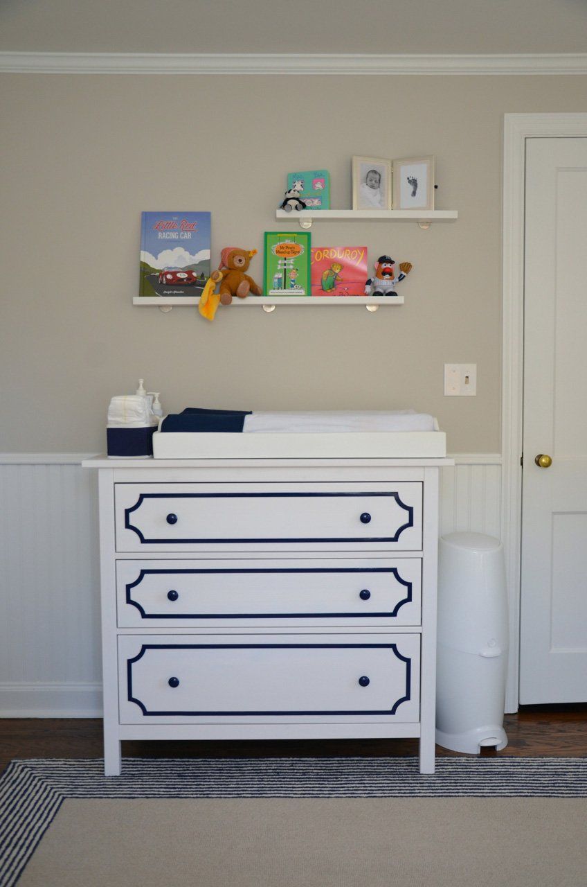 White changing table with navy trim, shelves with books and decor, next to a door.