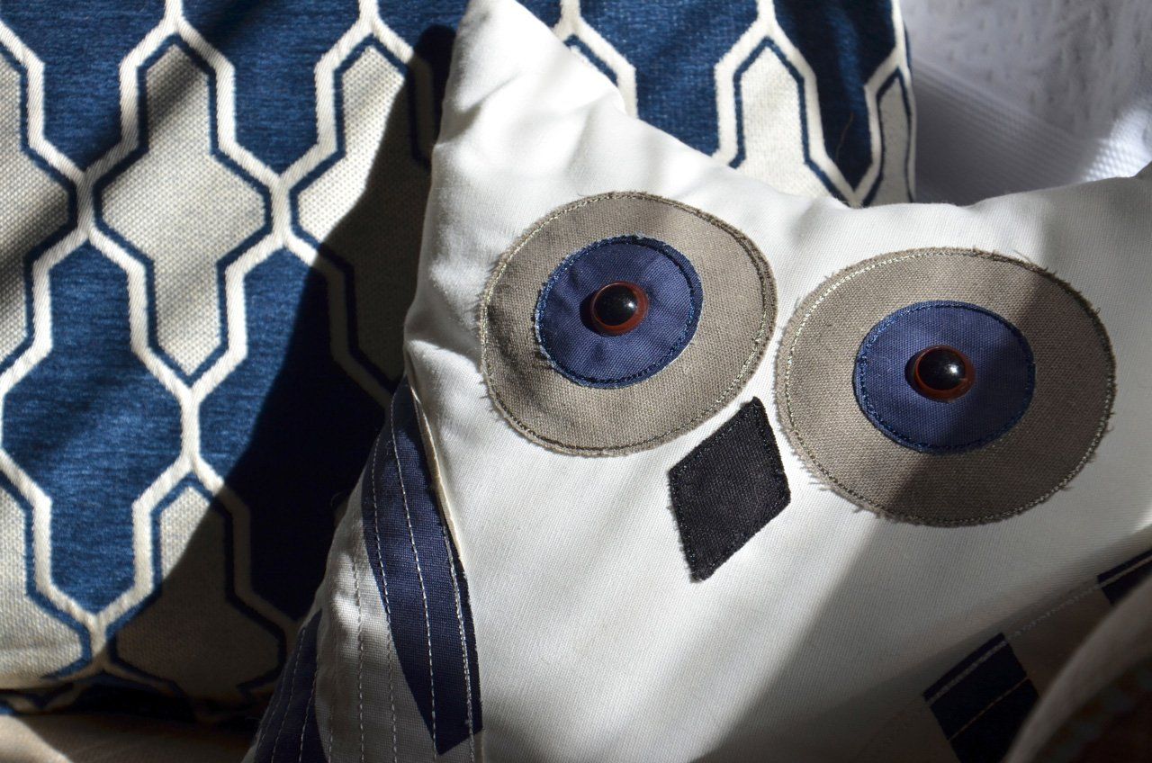 Owl-shaped white pillow with gray and blue accents, next to a blue patterned pillow.
