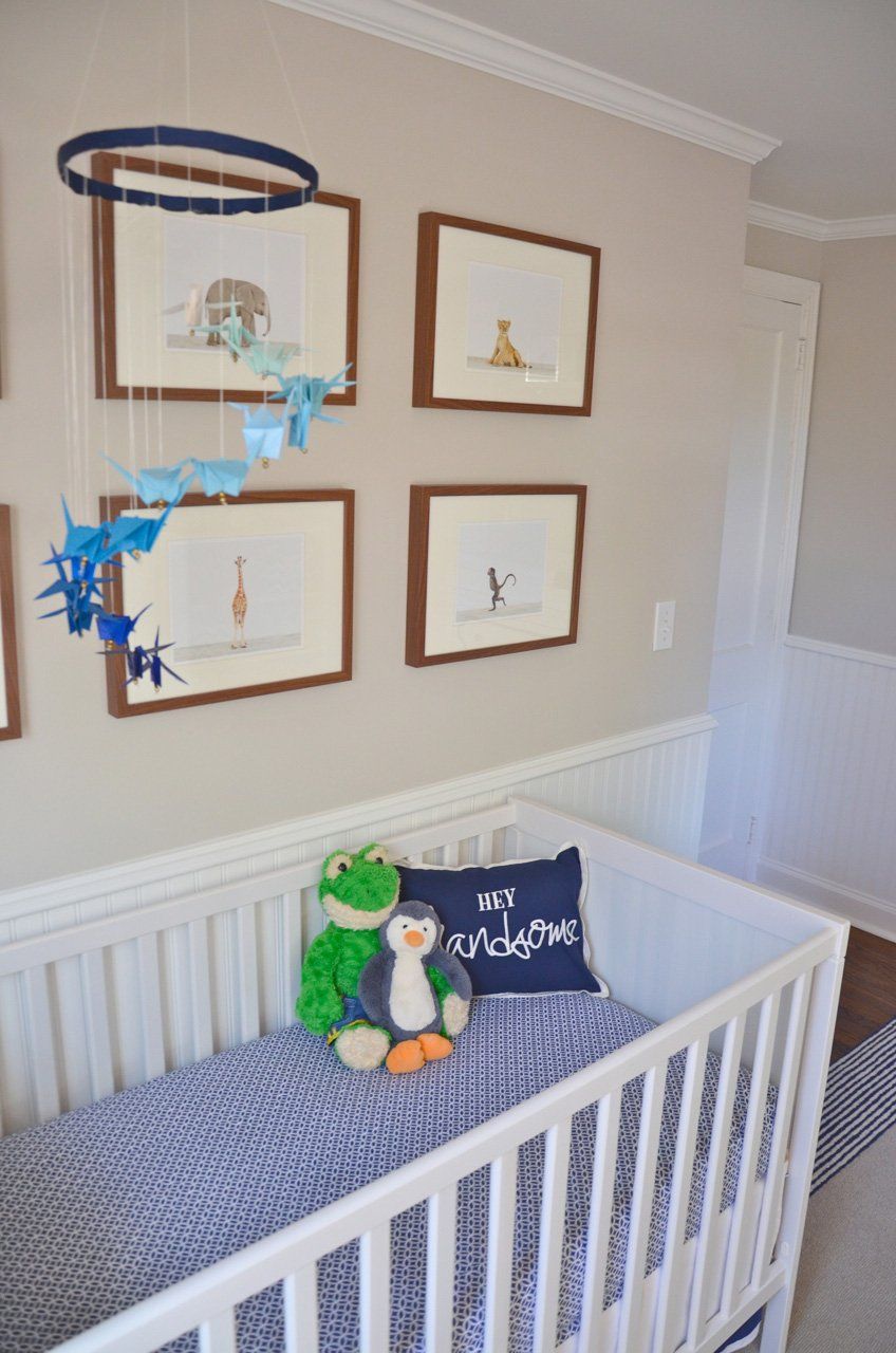 A nursery with a white crib, animal artwork, and a mobile. Blue and white color scheme.