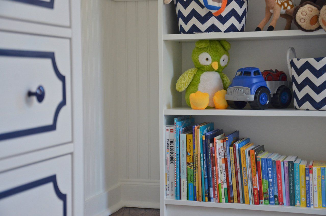 White bookshelf with toys and books, next to a white dresser with blue trim.