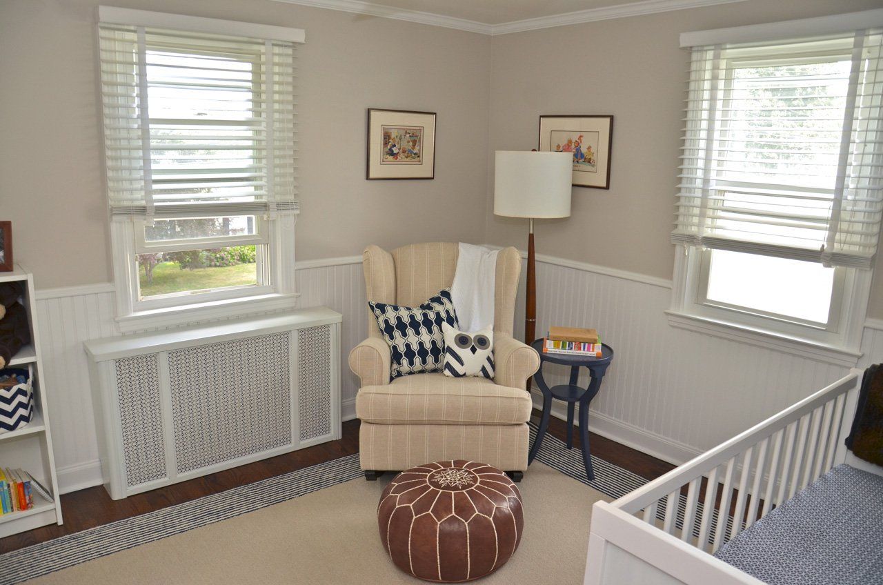 Cozy nursery with a white crib, armchair, and windows; neutral tones, soft lighting.