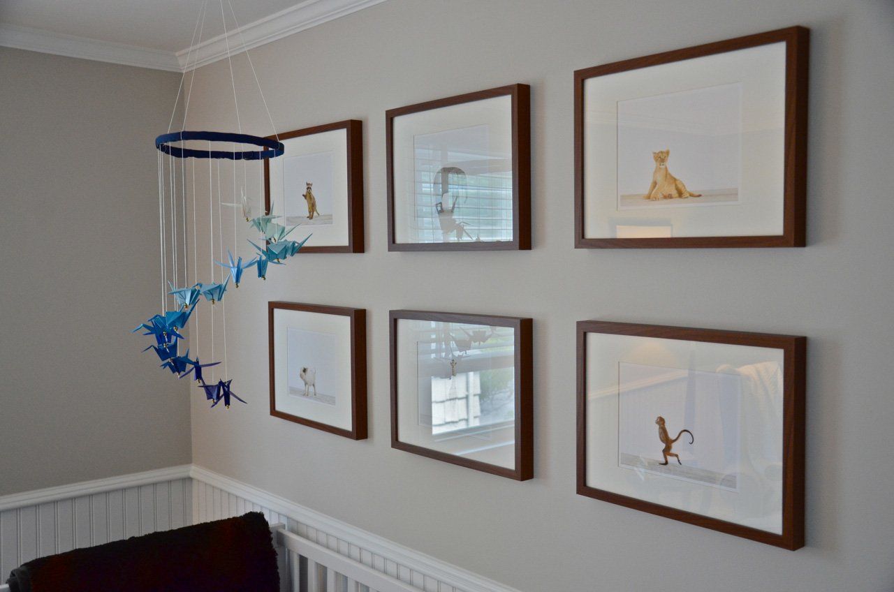 A nursery wall with framed illustrations and a hanging mobile; brown frames, blue and white decor.