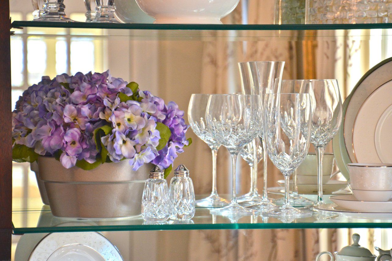 Glass cabinet shelf with purple flowers, crystal glasses, and china.