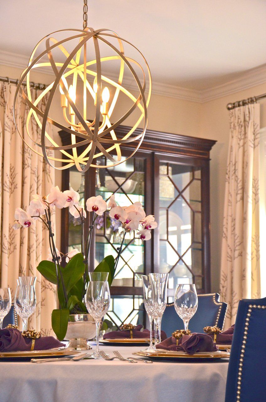 Dining room with table set for a meal; orchid centerpiece, globe light fixture, and china cabinet.