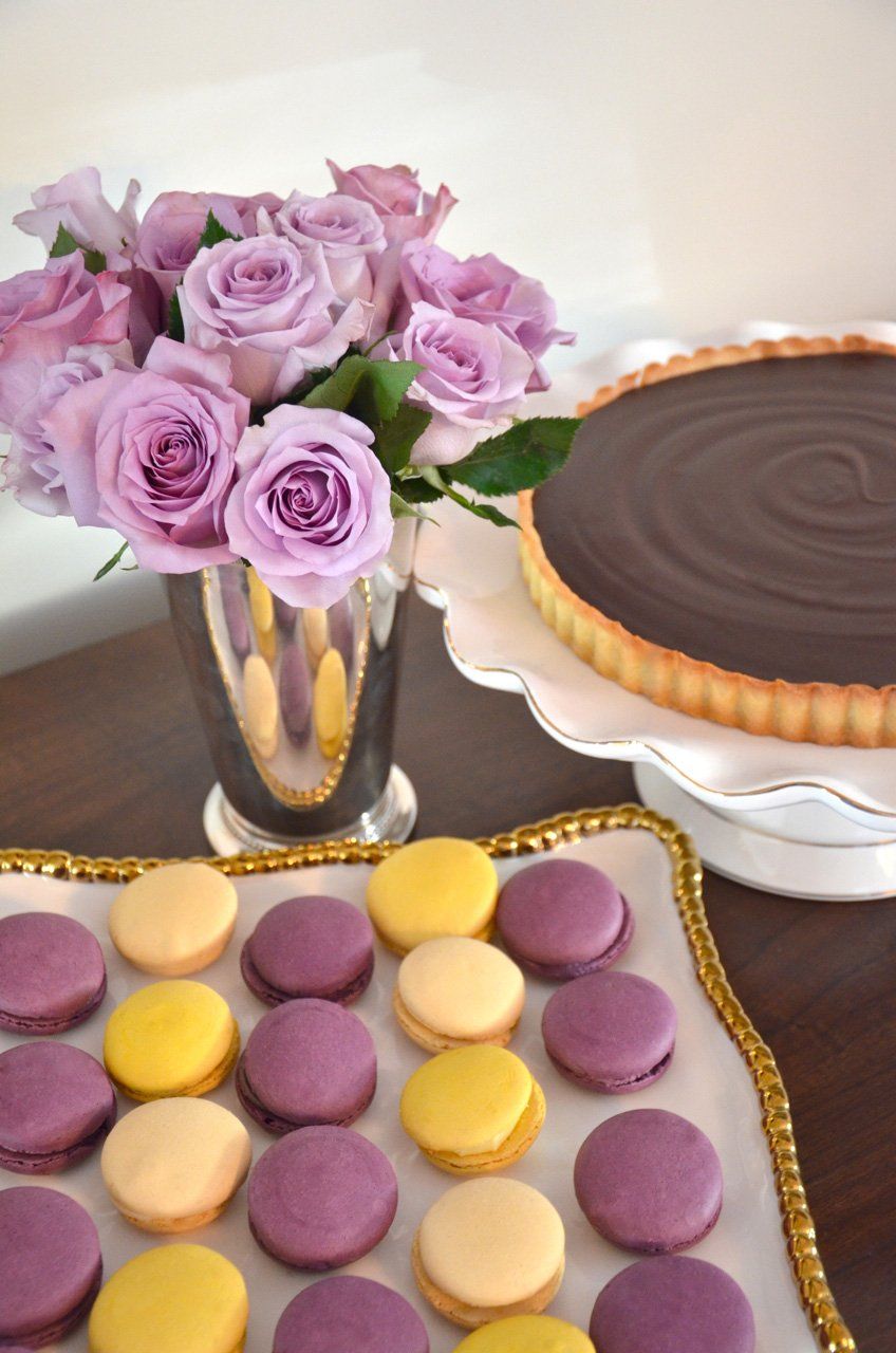 Bouquet of lavender roses, chocolate tart, and colorful macarons on a table.