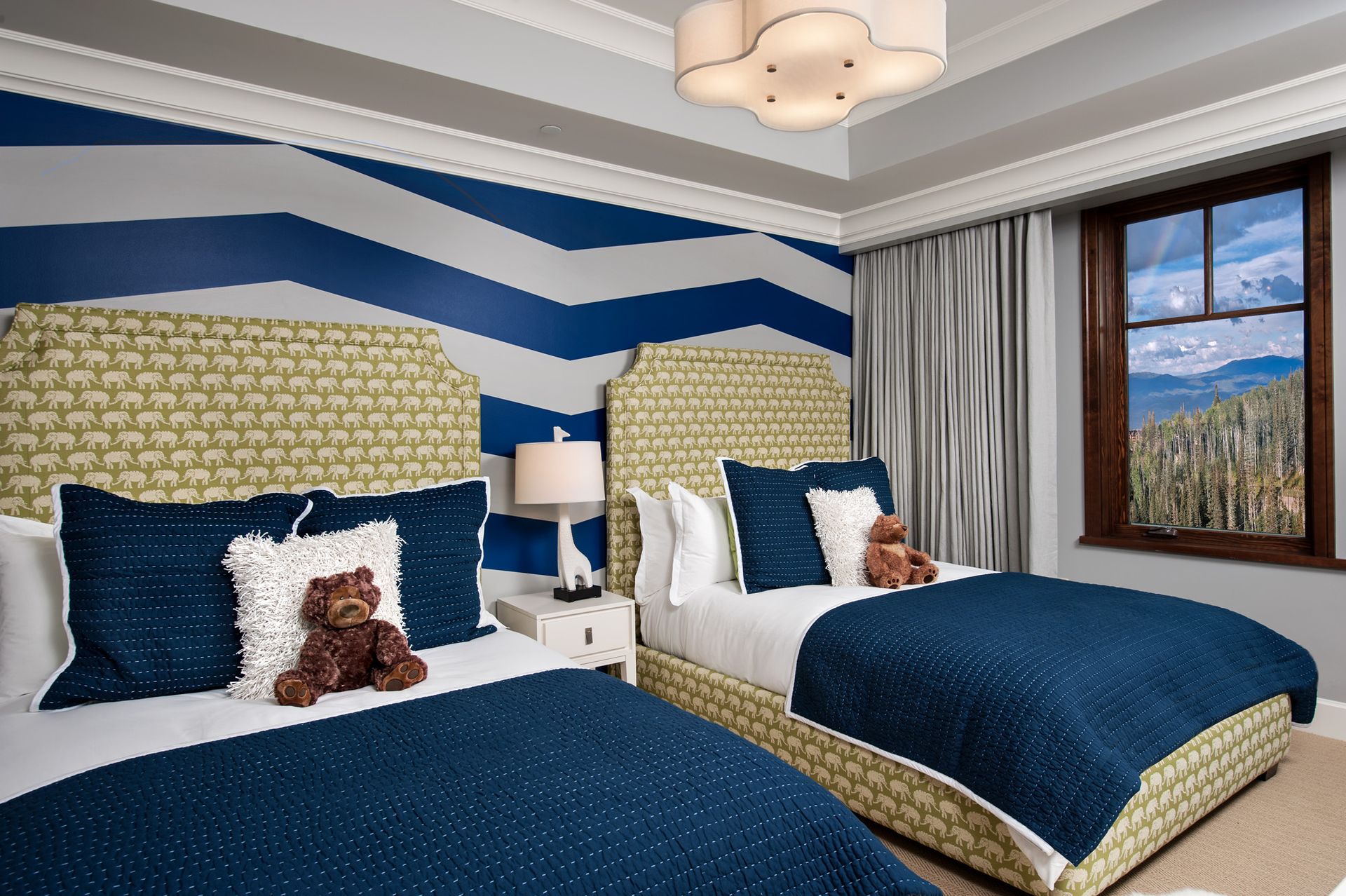 Twin beds in a bedroom with a blue and gray chevron-patterned accent wall and a scenic window view.