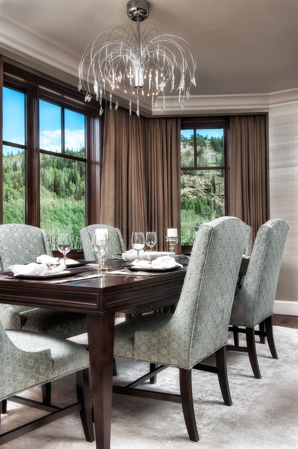Formal dining room: dark wood table, gray upholstered chairs, chandelier, windows with a view.