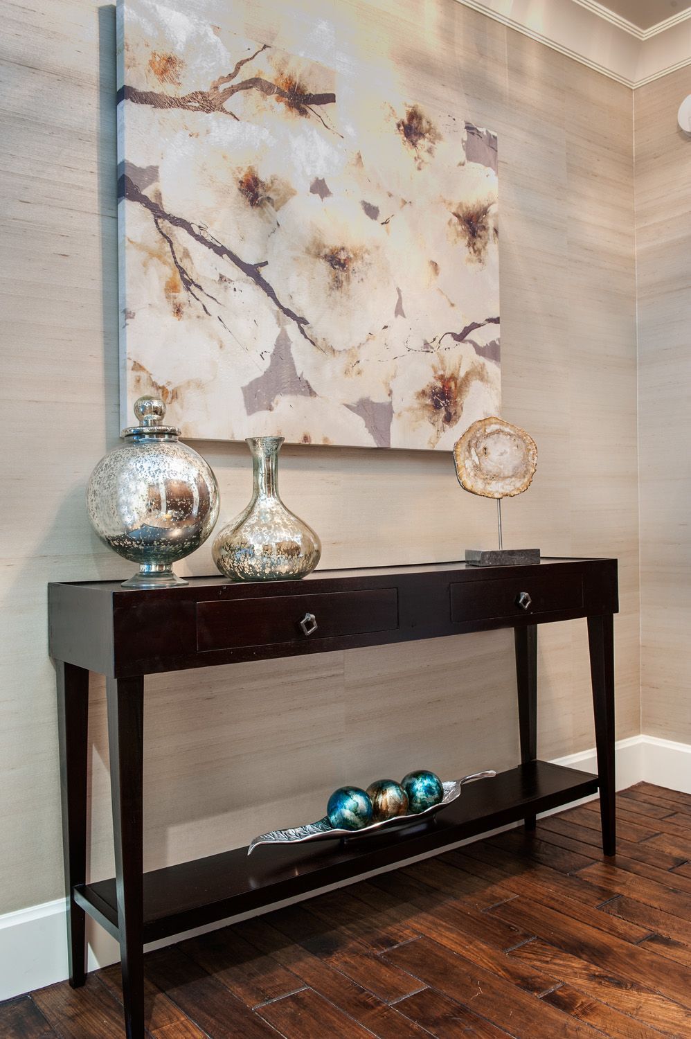 Dark brown console table with decorative vases beneath a floral painting, set against textured beige walls.