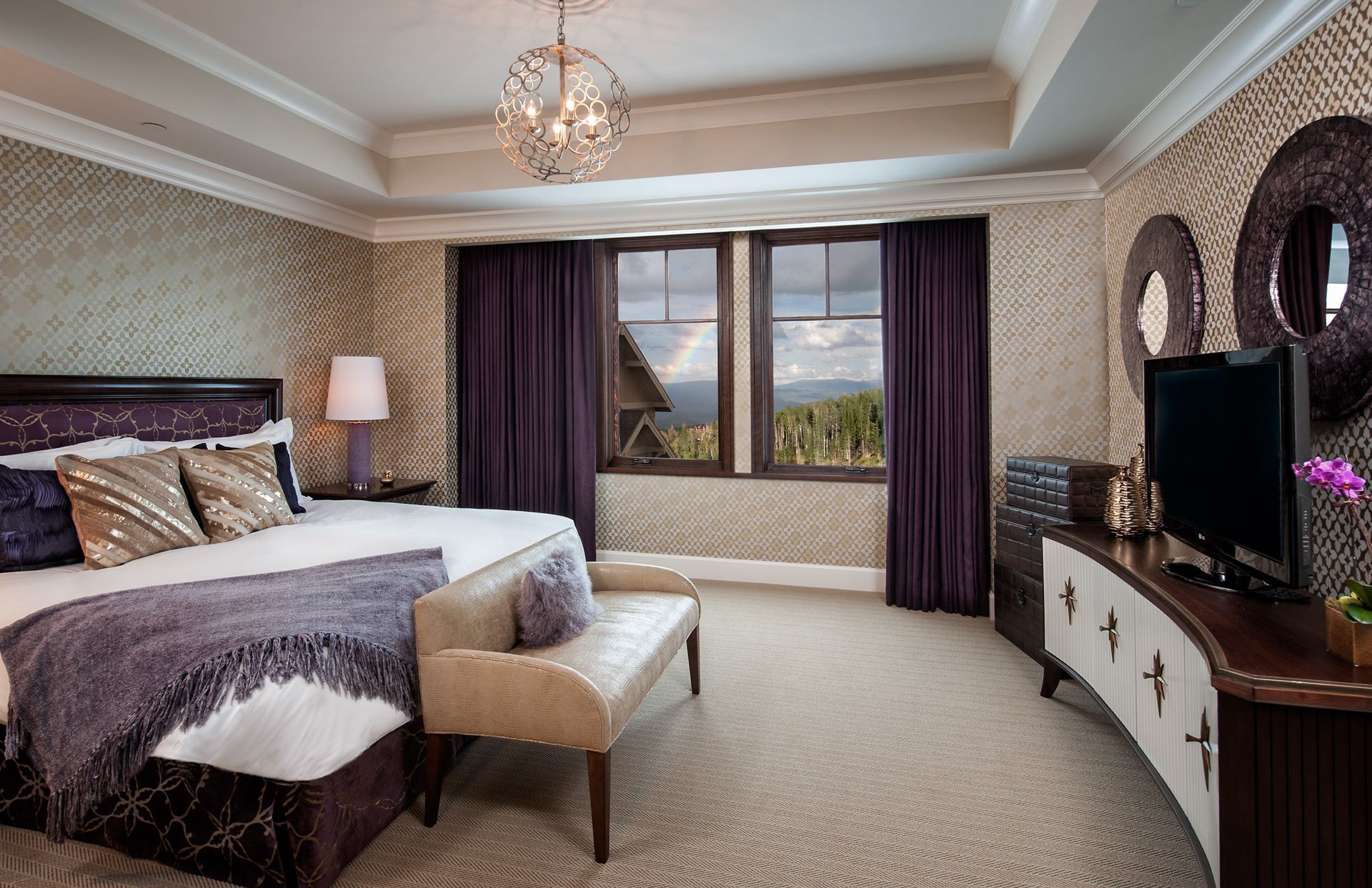 Elegant bedroom with purple accents, bed, bench, TV, and window with a mountain view.