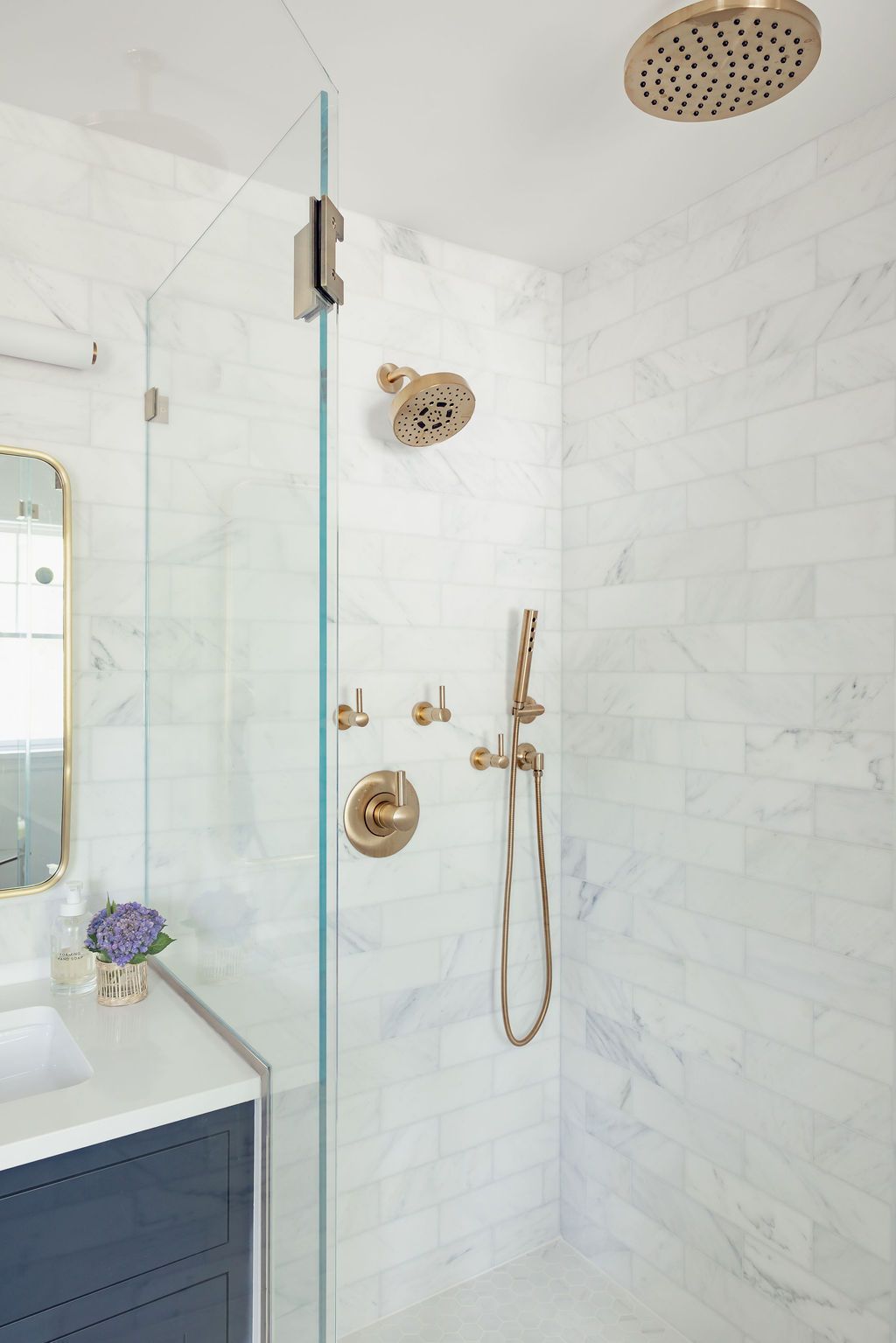 Shower with gold fixtures and white marble tile.