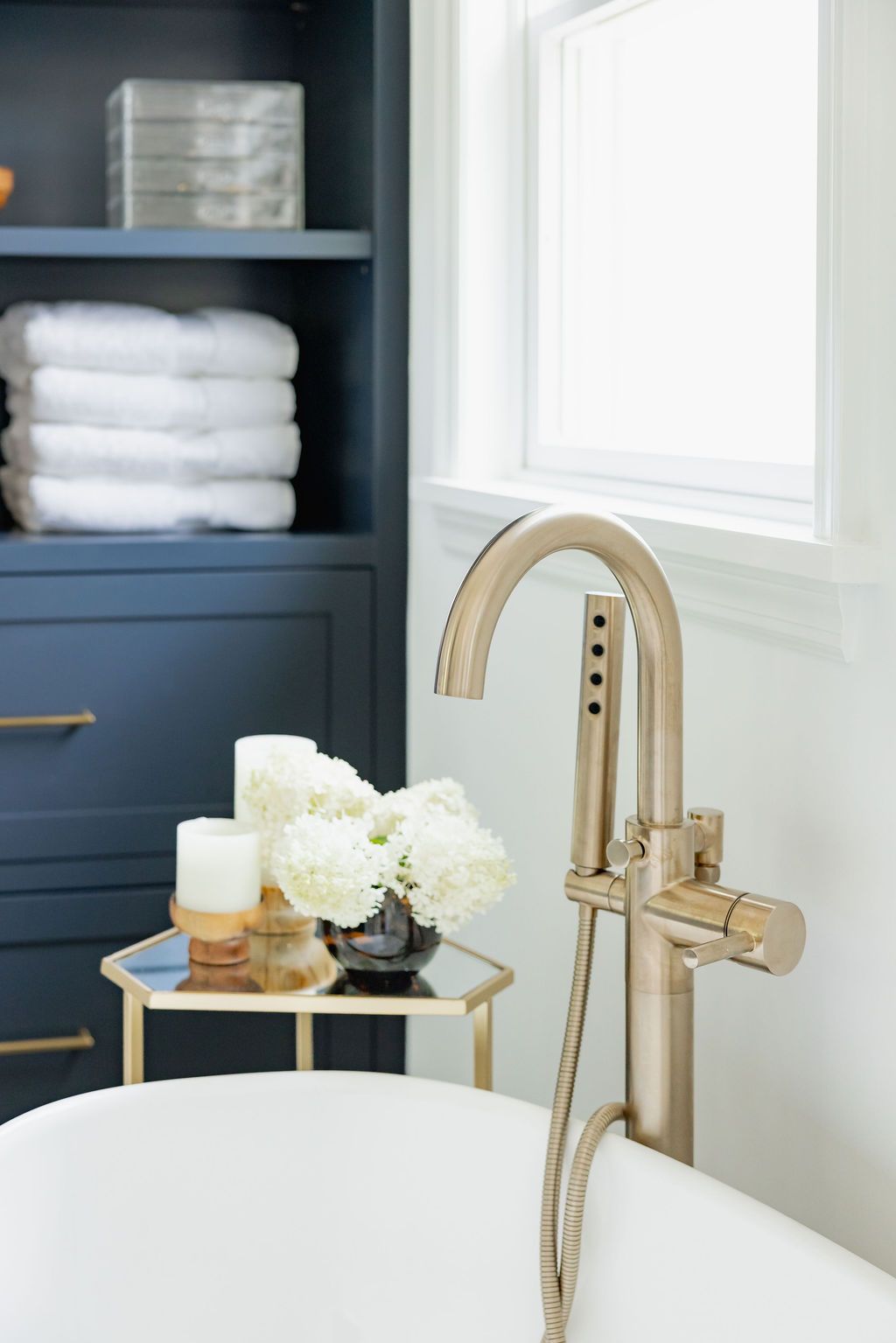 A modern bathroom with a freestanding bathtub and silver faucet. Navy blue cabinet with white towels and decor.