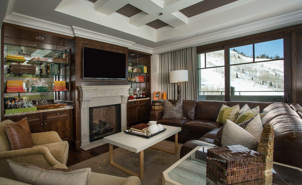 Living room with a fireplace, TV, and leather sofa overlooking a snowy mountain scene.