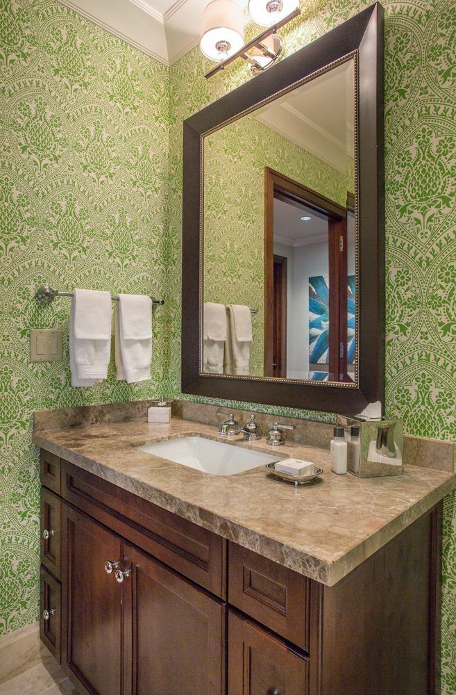 Bathroom with green patterned wallpaper, dark brown vanity, and large mirror.