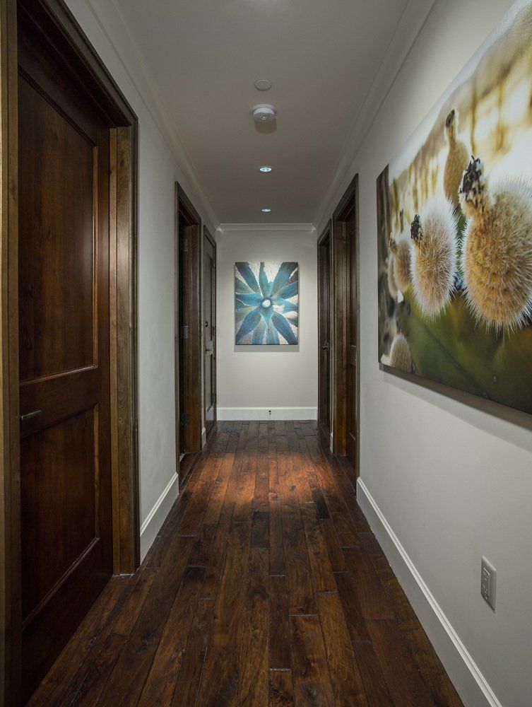 Long hallway with dark wood floor, doors, and artwork on white walls.