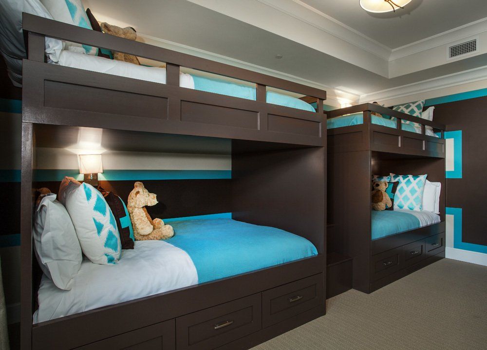 Two bunk beds in a room. Brown frames with blue bedding and accents. Light beige carpet.