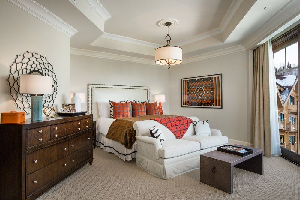 Elegant bedroom with a king-sized bed, white sofa, and a large window overlooking a snowy landscape.