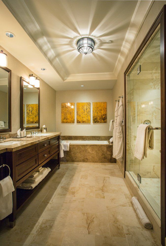 Luxurious bathroom with double vanity, bathtub, and glass shower. Earth-toned decor, ornate ceiling light.