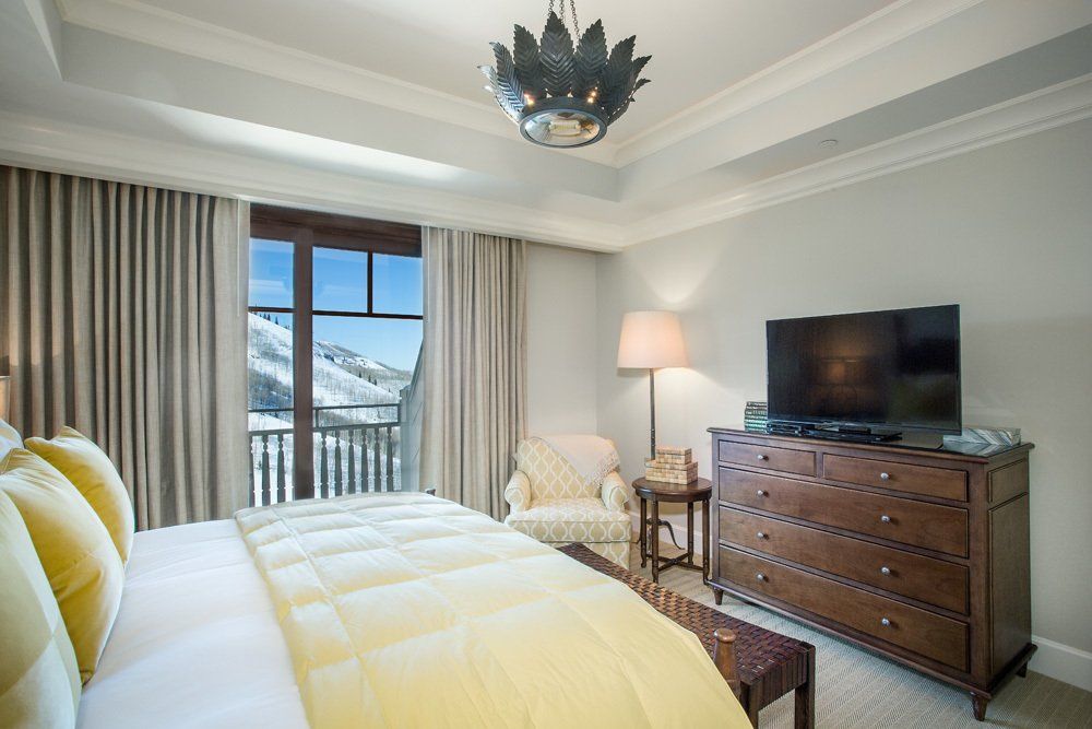 Bedroom with a bed, dresser, chair, large TV, and a window with a snowy mountain view.