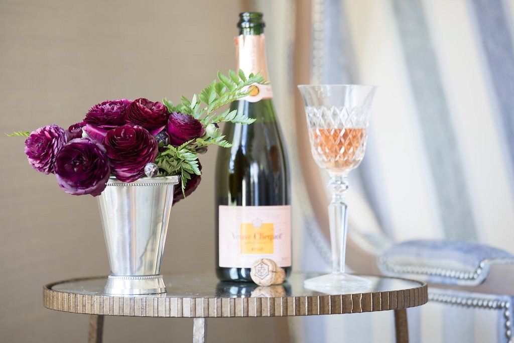 Champagne bottle and glass, flowers in a silver vase, on a mirrored table.